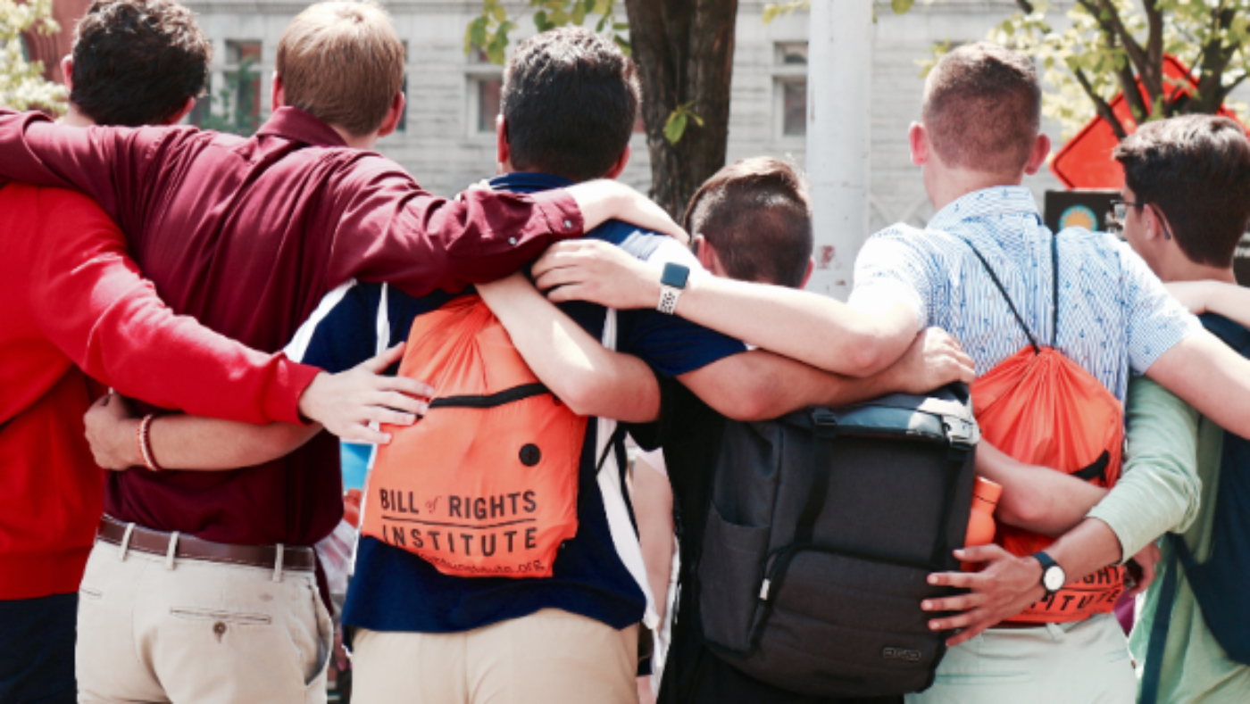 Group of people hugging, with one person wearing a 'Bill of Rights Institute' backpack.