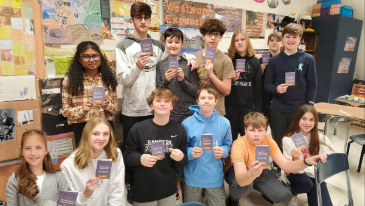 Classroom scene with students holding pocket Constitutions, a chalkboard with text, and educational posters.